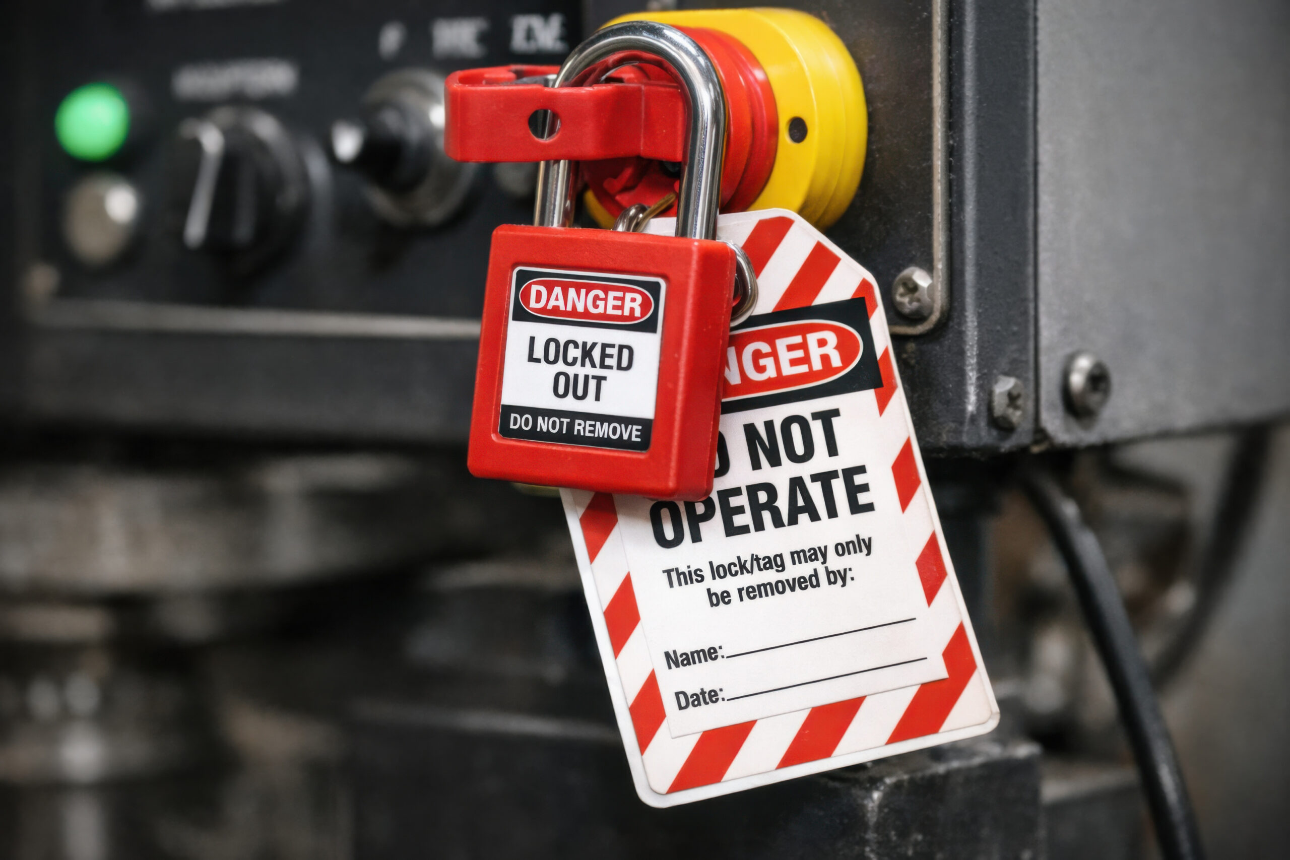 Close up of lockout safety system with red padlock and warning label. tag hangs on heavy machinery control, representing serious workplace safety compliance concept